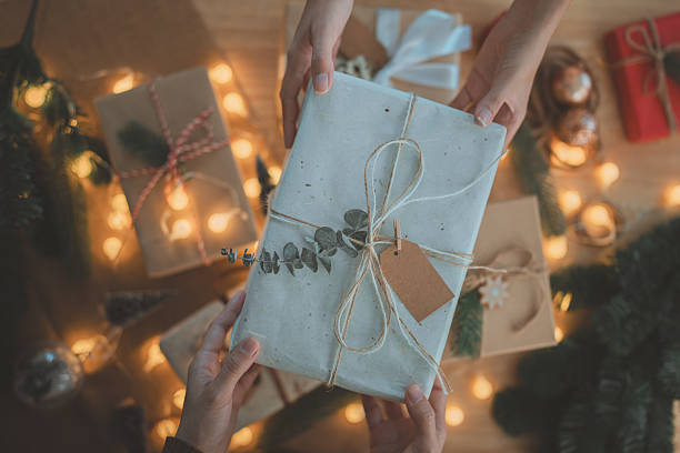 istock Christmas gift exchange with hands holding a beautifully wrapped present decorated with natural twine and pine twig, symbolizing festive giving, warmth, celebration, and holiday tradition 2248214534