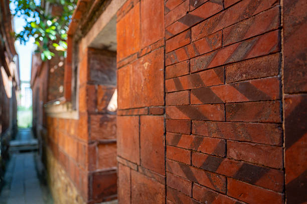 A narrow alleyway between two brick buildings, illuminated by sunlight filtering through gaps, creating a warm and inviting atmosphere. The scene captures the interplay of light and shadow on textured surfaces, offering a sense of depth and perspective. Potential usage includes architectural studies, urban photography, or artistic inspiration.