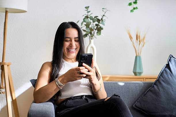 istock Young woman relaxing on sofa laughing at phone screen 2248217959