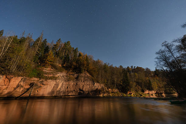Scenic Night Landscape in Gauja National Park, Latvia with Devonian Sandstone Cliffs, River Reflection and Starry Blue Sky