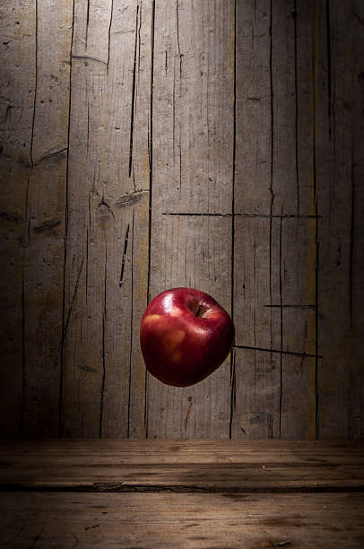 istock Apple floats in front of wood texture, zenithal light above highlights it, casting a subtly displaced shadow below and behind. 2248227424