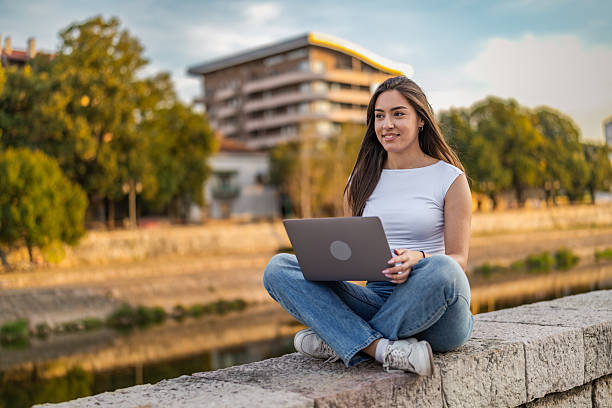 istock Beautiful girl with long hair freelancer work while sitting and using laptop on quayside in the city near the river. 2248236077