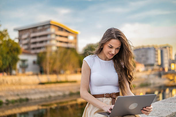 istock Beautiful girl with long hair freelancer work while sitting and using laptop on quayside in the city near the river. 2248236326