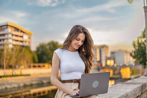 istock Beautiful girl with long hair freelancer work while sitting and using laptop on quayside in the city near the river. 2248236549