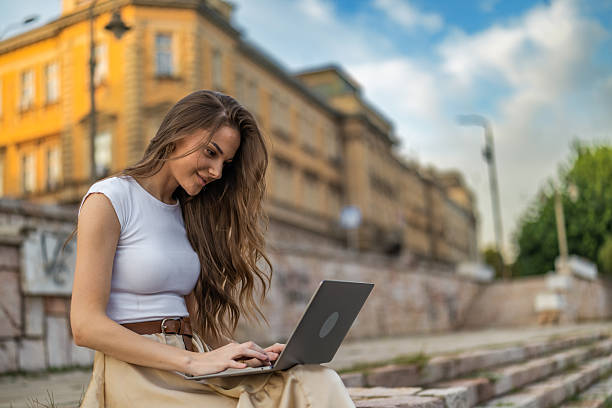 istock Beautiful girl with long hair freelancer work while sitting and using laptop on quayside in the city near the river. 2248236571