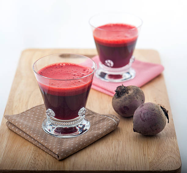 Two glasses of vibrant red beetroot juice served on a rustic wooden board with fresh whole beets. Clean, bright studio shot ideal for healthy eating, detox, superfood and wellness stock photography.