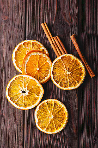Dried orange slices and cinnamon sticks lie on a dark wooden surface with ample copy space. Warm tones and natural textures create a cozy, festive mood suitable for seasonal designs, crafts, and holiday-themed projects.