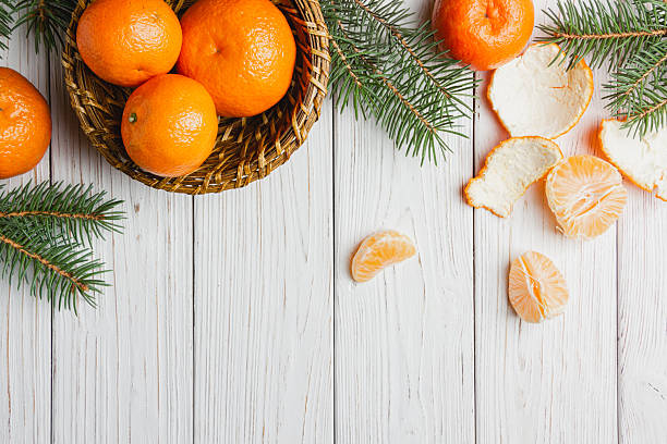 istock Tangerines in a straw basket with spruce branches on a white wooden table. 2248241944
