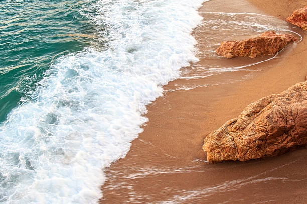 Foam from the wave breaking on the shore of the sandy beach with rocks