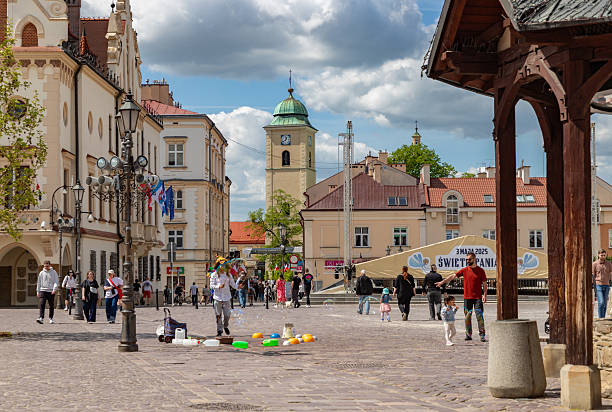 Rzeszow, Poland - May 1, 2025: A picture of a street performer creating large soap bubbles at the main square of Rzeszow, with the tower of the Church of Saint Adalbert and Saint Stanislaus visible afar.