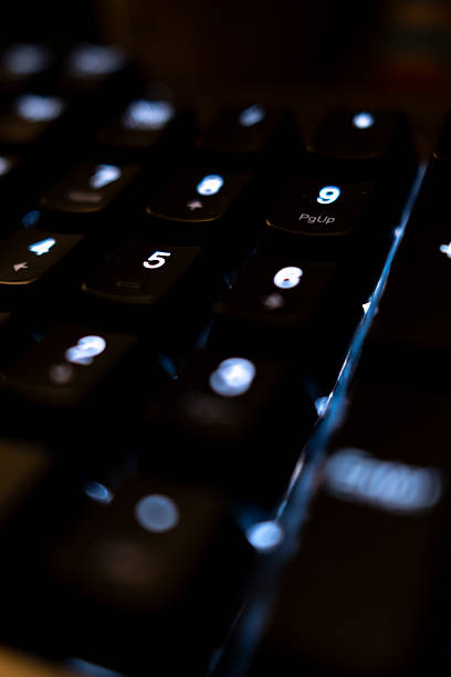 A detailed macro view of a computer keyboard illuminated with blue LED backlighting, highlighting symbols and numbers for a technology and digital culture concept.