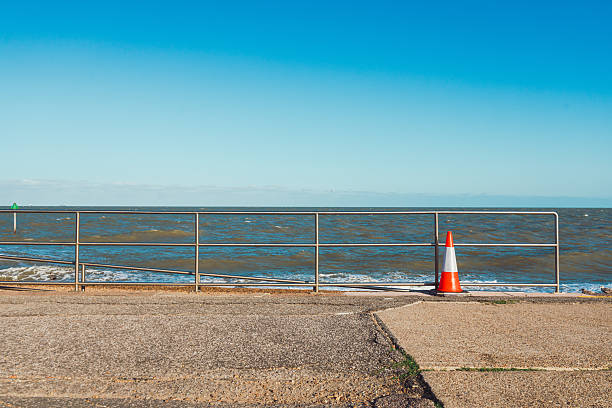 Orange and white traffic cone standing near a metal railing on the coast of felixstowe, england
