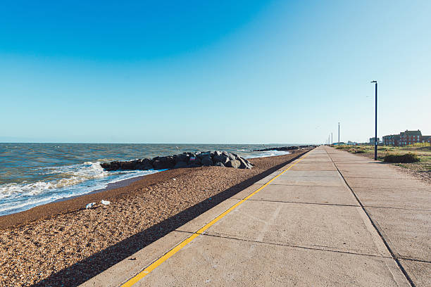A pebble beach with a sea horizon on a sunny day, and a lone and unrecognisable surfer in the mid-distance.