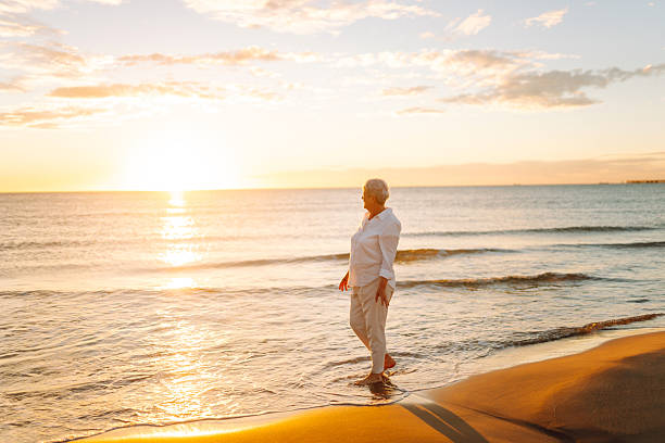 istock A joyful elderly woman feels free as she strolls along a sandy beach at sunset. 2248250556