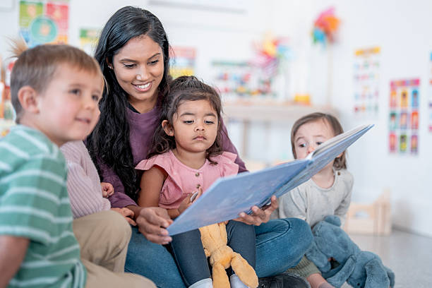 istock Diverse Female Caregiver Reading With Children In Classroom Library 2248253100