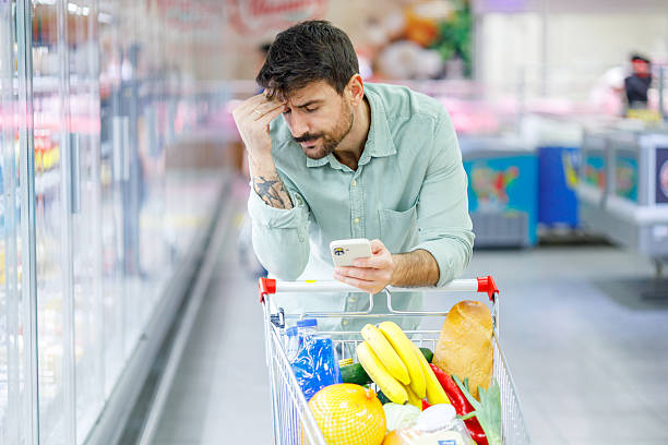 istock Worried man checking prices on smartphone while grocery shopping, experiencing financial stress and inflation concerns 2248253444