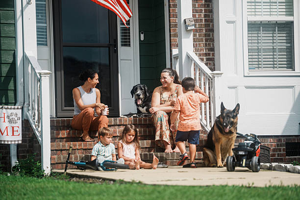 Two women sit and chat on the front steps of a North Carolina home while their young children and family dogs play together on a warm summer afternoon.