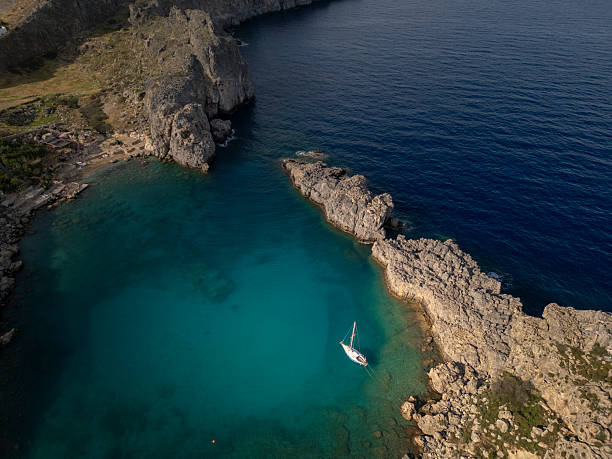 Sailboat anchored in a secluded turquoise bay on rhodes island, greece, with rugged cliffs and clear mediterranean sea water perfect for summer holidays and travel