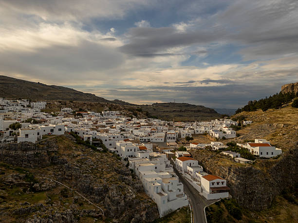 Lindos village clustering on a hillside. Showcasing its iconic whitewashed houses and ancient acropolis against a dramatic sky. Representing mediterranean travel and historical sites on rhodes island