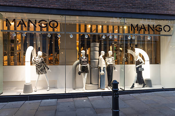 Illuminated Mango fashion boutique window with mannequins and trendy outfits, viewed from the street at night in an urban shopping district. London, UK, 2 September 2023