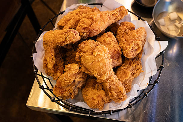Crispy Korean fried chicken pieces served in a black wire basket with parchment paper on a metal table