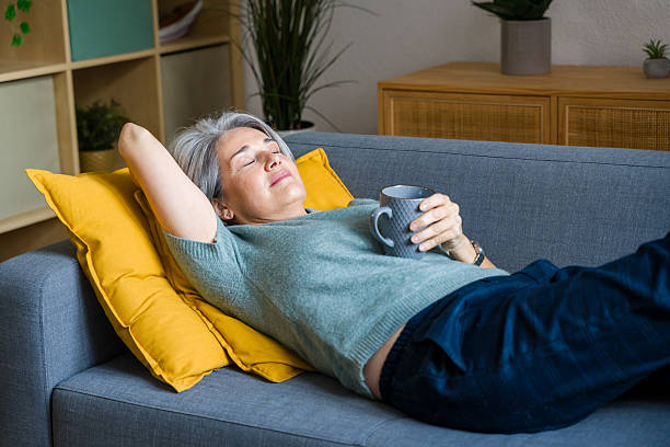 istock Mature woman relaxing on sofa holding cup at home 2248259091