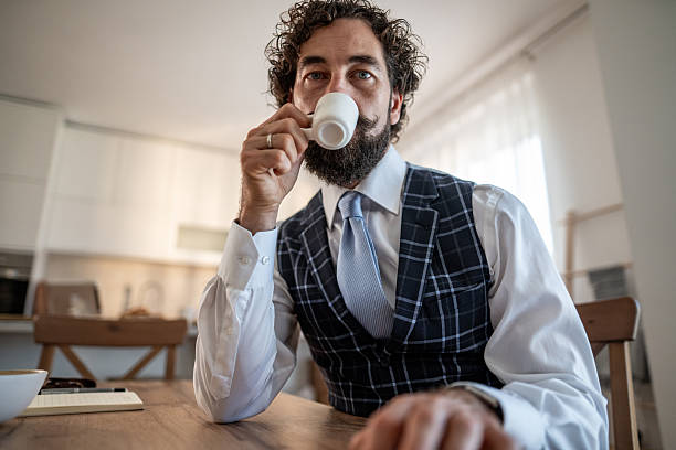 Professional man enjoying an espresso while sitting at a kitchen table, contemplating business ideas in a home office environment, embodying a relaxed yet productive work-from-home lifestyle