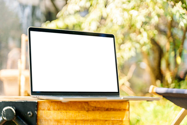 Modern laptop with empty white screen placed on wooden table in park. Mockup concept for web design, business presentation, advertising, app showcase, digital marketing, and online communication. Copy space for text or graphics.