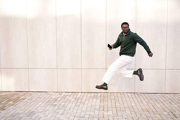 istock Black man jumping and holding mobile phone 2248267818