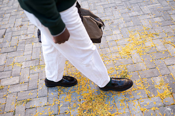 Man walking confidently down cobblestone street carpeted with yellow autumn leaves, carrying travel bag and heading onward