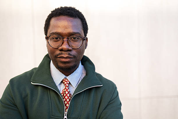 Portrait of a confident black man wearing glasses, a striped shirt, patterned tie, and dark green fleece