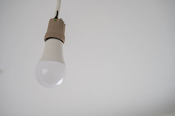 istock Minimalist close-up of a hanging LED light bulb with an exposed socket against a plain white ceiling. 2248271130