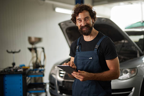 istock Car mechanic using digital tablet, smiling at camera in auto repair shop 2248275050
