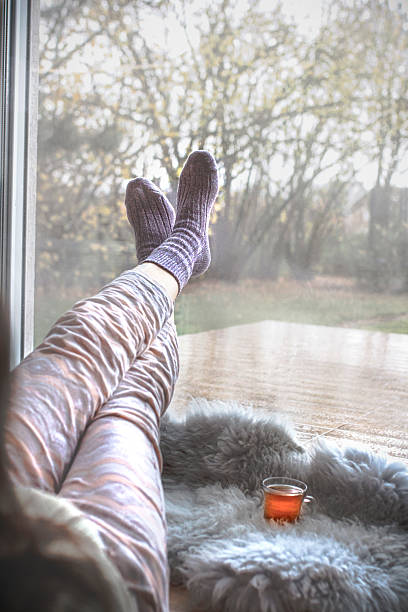 istock Feet in soft socks resting by window with tea on rainy day 2248275694