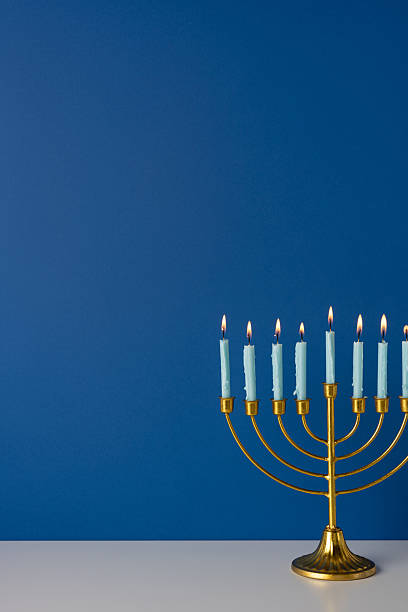 istock Gold vertical menorah with lit candles sits on a white table against a deep blue backdrop, capturing Hanukkah warmth, tradition, and festive mood suitable for holiday greeting and celebration imagery 2248277584