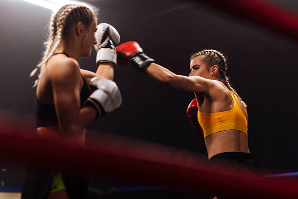 Two female athletes spar in a boxing ring, one delivering a punch toward the other