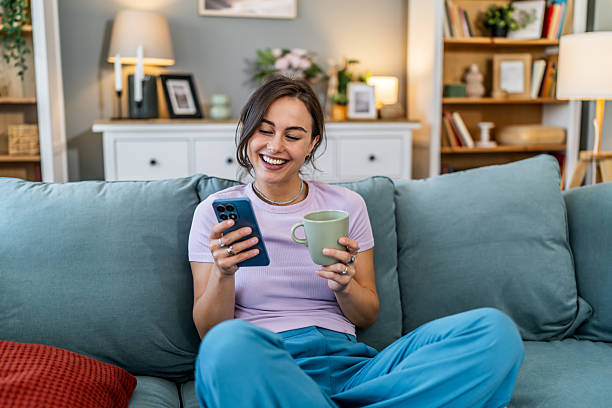 istock Young woman laughing, using smartphone, relaxing on couch 2248281110