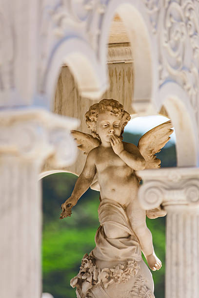 istock Child angel sculpted in light marble, framed between ornate columns and arches, with a blurred green background highlighting its form. Unknown artist, São João Batista Cemetery, Rio de Janeiro, Brazil. 2248282871