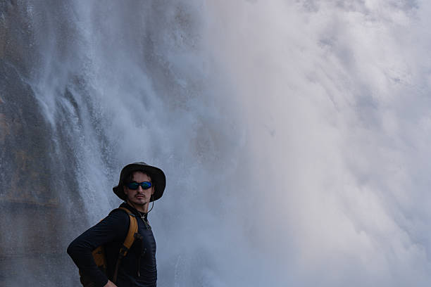 istock Explorer poses before a grand waterfall, clad in hat and stylish sunglasses. 2248284000