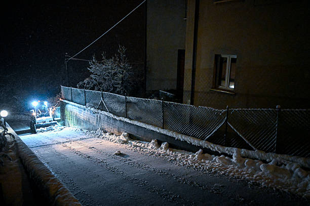 Small snow plow clearing snow from a residential street at night during winter