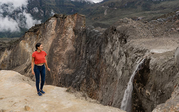 Woman standing on cliff edge, admiring rugged canyon landscape and waterfall