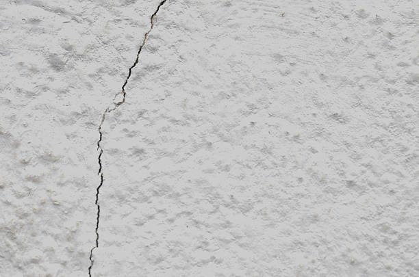 Prominent dark vertical crack on a rough, stippled white plaster wall, symbolizing structural damage, aging infrastructure, and the urgent need for home repair or renovation.