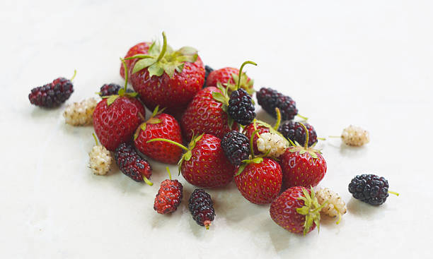 There are white and red mulberries and strawberries on the table.