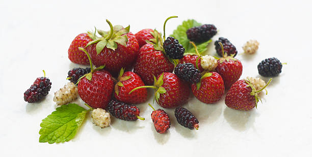 There are white and red mulberries and strawberries on the table.
