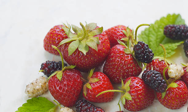 There are white and red mulberries and strawberries on the table.