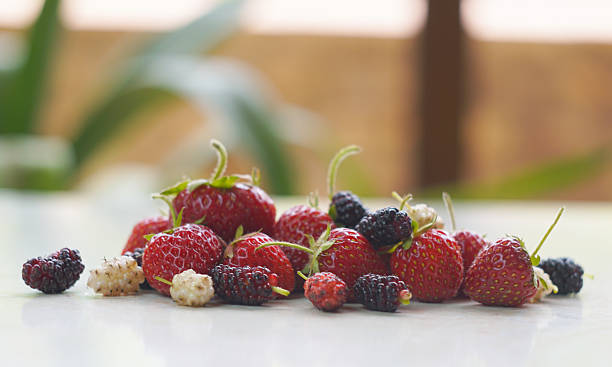 There are white and red mulberries and strawberries on the table.