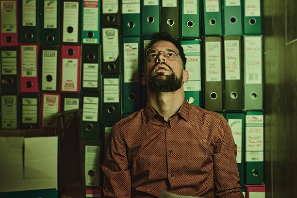 Portrait of exhausted male entrepreneur day dreaming against file folders in the office.
