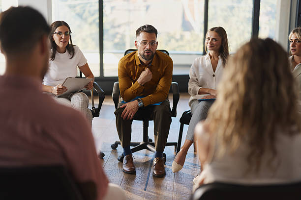 istock Young businessman talking to a coach on a group therapy in the office. 2248317192