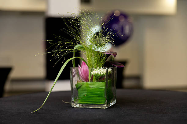 A sophisticated floral centerpiece featuring lush greenery and a hint of pink blossoms in a modern glass vase. perfect for adding a touch of elegance to any occasion or decor.