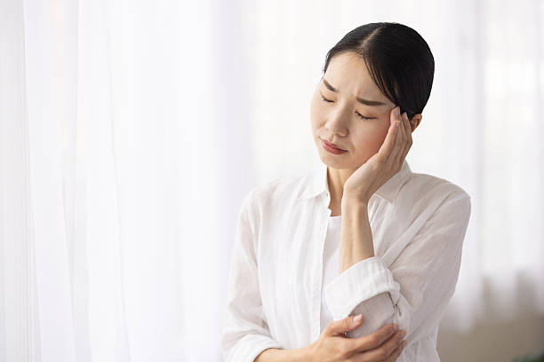 istock Woman Standing by Window Touching Temple with a Painful Expression 2248323451